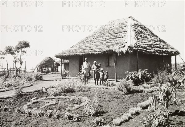A Kikuyu family outside their home. A Kikuyu family pose in the garden outside their new, Western-style house. South Nyeri, Kenya, 1936. Nyeri, Central (Kenya), Kenya, Eastern Africa, Africa.