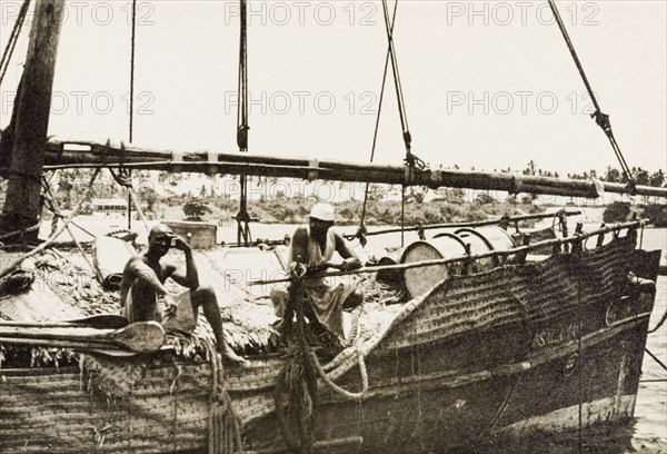 Dhow in Old Mombasa harbour. Two men perch on the edge of a dhow moored in Old Mombasa harbour. Mombasa, Kenya, 1933. Mombasa, Coast, Kenya, Eastern Africa, Africa.