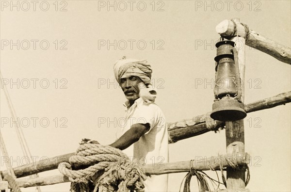 Sailor with a seabird. A turbaned dhow captain stands on the deck of his boat with a seabird resting on his shoulder. Malindi, Kenya, 1947. Malindi, Coast, Kenya, Eastern Africa, Africa.