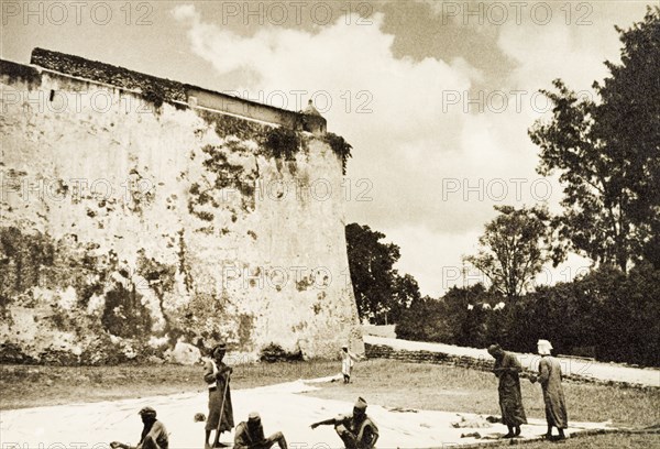 Sail makers repairing a dhow sail. A number of sail makers repair a large dhow sail on an open patch of ground below Fort Jesus. Mombasa, Kenya, 1933. Mombasa, Coast, Kenya, Eastern Africa, Africa.