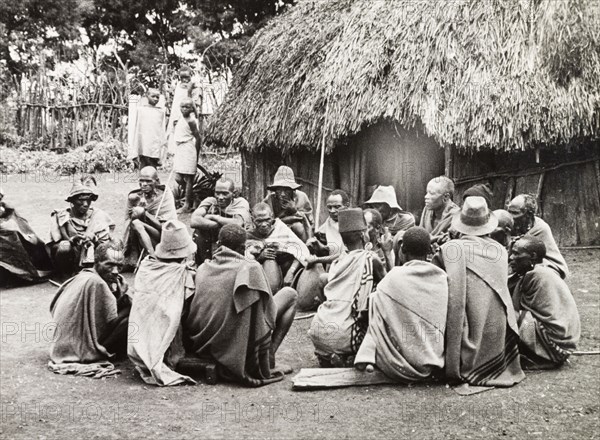 A meeting of Kikuyu elders. A group of Kikuyu men gather in a circle to drink beer from a hollow bullock's horn, a privilege granted only to tribal elders. Nyeri, Kenya, 1936. Nyeri, Central (Kenya), Kenya, Eastern Africa, Africa.