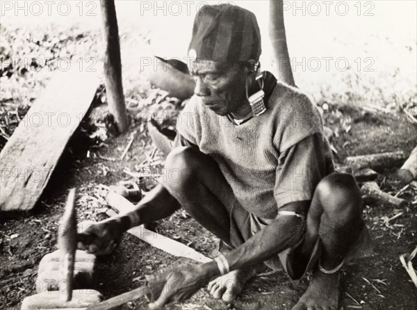 A Kikuyu metalsmith. A Kikuyu metalsmith hammers a knife blade into shape using an anvil in his workshop. Nyeri, Kenya, 1936. Nyeri, Central (Kenya), Kenya, Eastern Africa, Africa.