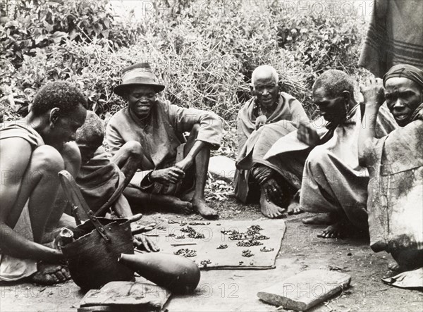 Telling fortunes by beans'. A group of Kikuyu men gather around to read their fortunes by scattering beans on the ground. South Nyeri, Kenya, 1936. Nyeri, Central (Kenya), Kenya, Eastern Africa, Africa.