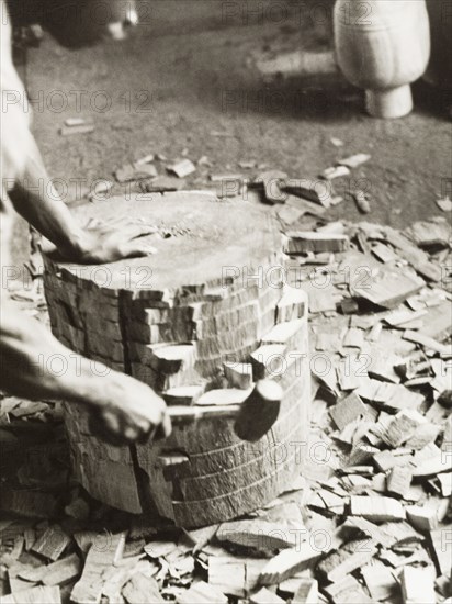Shaping the shell of an atumpan drum. A craftsman uses a mallet on a section of timber, knocking out small blocks of wood to shape the shell of an atumpan drum. Ghana, circa 1965. Ghana, Western Africa, Africa.