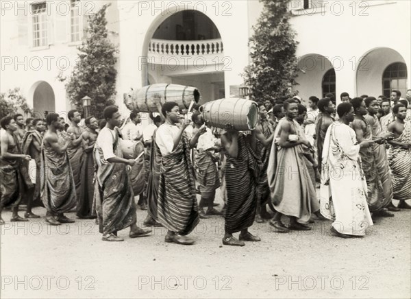 Procession for Foundation Day, Accra. Students of Achimota School in Accra form a procession to celebrate Foundation Day. Two students carry atumpan drums on their shoulders as drummers beat the drumheads from behind with curved sticks. Accra, Ghana, circa 1965. Accra, East (Ghana), Ghana, Western Africa, Africa.