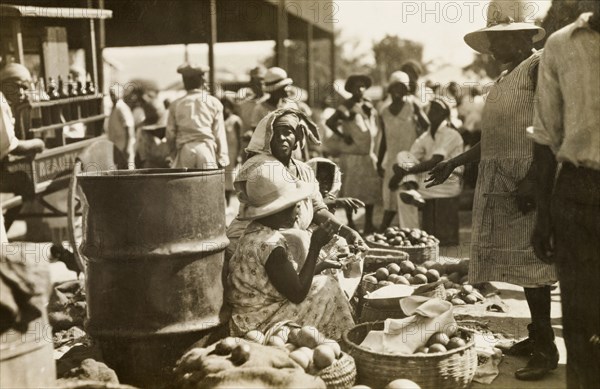 Street traders at a Jamaican market. Female street traders sell fruit, vegetables and smoked fish from baskets at an outdoor market. Jamaica, circa 1925. Jamaica, Caribbean, North America .