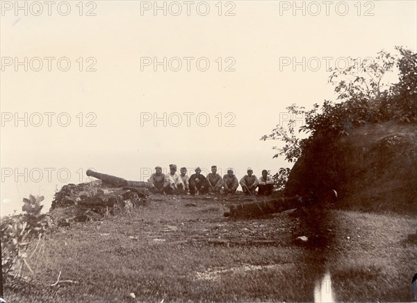 A bastion on Anjidiv Island. A row of men sit beside two cannons on the eastern bastion of a fortification on Anjidiv Island. Near Goa, India, circa 1890., Goa, India, Southern Asia, Asia.