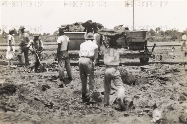 Transporting asphalt from the Pitch Lake. Labourers load lumps of asphalt extracted from Trinidad's Pitch Lake onto a waiting rail car. La Brea, Trinidad, circa 1931. La Brea, Trinidad and Tobago, Trinidad and Tobago, Caribbean, North America .