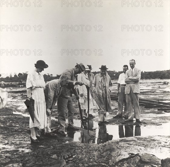 Visitors to the Pitch Lake. Several European friends visit the Pitch Lake, a natural asphalt lake located on Trinidad's west coast. One of the group pokes his umbrella inquisitively into a puddle on the surface. La Brea, Trinidad, circa 1939. La Brea, Trinidad and Tobago, Trinidad and Tobago, Caribbean, North America .