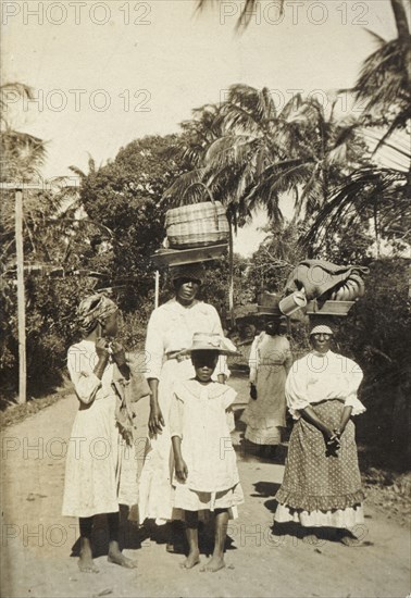Returning from market, Tobago. A group of women and girls return from a local market balancing baskets of goods on their heads. An original caption suggests the tall woman in the centre is a cook by trade. Tobago, circa 1912., Trinidad and Tobago, Trinidad and Tobago, Caribbean, North America .