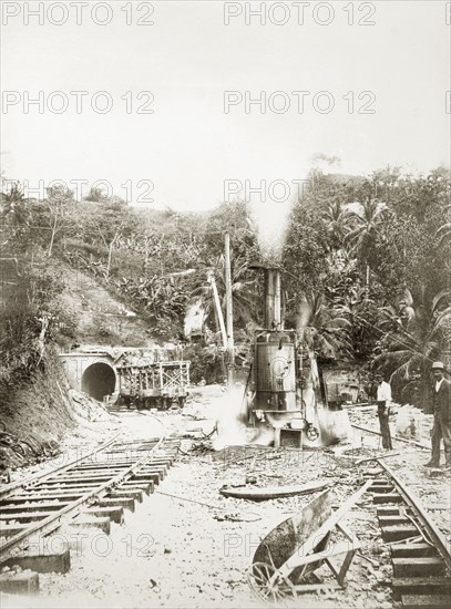 Railway construction site. Labourers stand on the tracks beside steam-operated machinery at a railway construction site. Jamaica, circa 1895. Jamaica, Caribbean, North America .