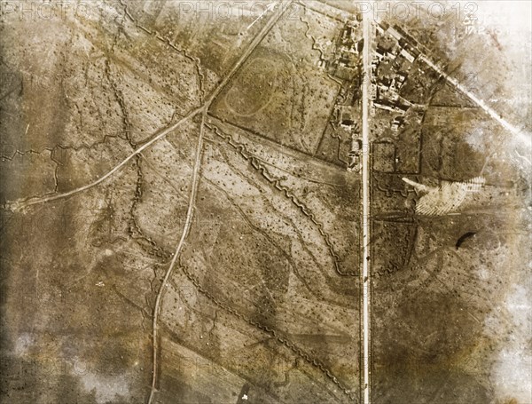 Trenches surround a bomb-damaged village. One of a series of British aerial reconnaissance photographs recording the positions of trenches on the Western Front during the First World War. Square-toothed trenches zig-zag across fields pockmarked with bomb craters on the outskirts of a small village. A prominently straight road appears to the right, possibly one of several Roman roads in the region. Nord-Pas de Calais or Picardie, France, 17 February 1918., Nord-Pas de Calais, France, Western Europe, Europe .