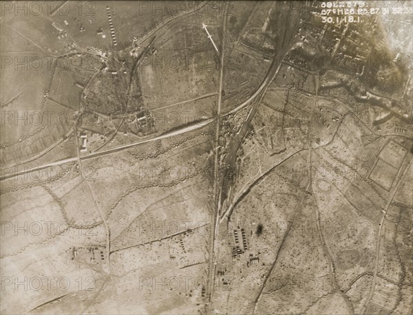 A military camp at a bomb-damaged village. One of a series of British aerial reconnaissance photographs recording the positions of trenches on the Western Front during the First World War. Sqaure-toothed trenches encircle a military camp, probably British, on the outskirts of a bomb-damaged village. The surrounding fields are peppered with shell blasts after suffering a continuous barrage of artillery fire. Nord-Pas de Calais or Picardie, France, 30 January 1918., Nord-Pas de Calais, France, Western Europe, Europe .