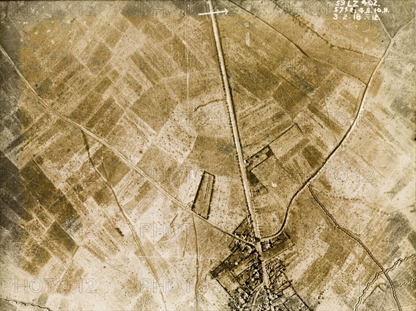 Aerial view of a bomb-damaged village. One of a series of British aerial reconnaissance photographs recording the positions of trenches on the Western Front during the First World War. A prominently straight road, possibly one of several Roman roads in the region, runs east to west through a bomb-damaged village, surrounded by fields pockmarked with bomb craters. Nord-Pas de Calais or Picardie, France, 3 February 1918., Nord-Pas de Calais, France, Western Europe, Europe .