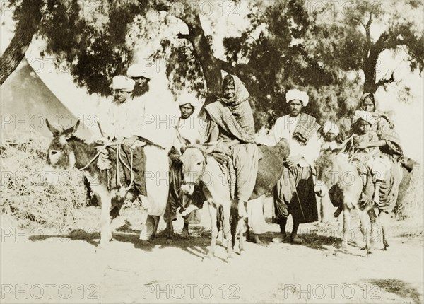 Indian family travelling by donkey. An Indian family travel along a rural road: some riding donkeys, others on foot. India, circa 1910. India, Southern Asia, Asia.