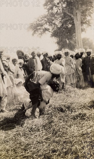 Wrestling match in Sukkur . A crowd of spectators gathers to watch a wrestling match in a grassy arena. Sukkur, India (Pakistan), 1926. Sukkur, Sindh, Pakistan, Southern Asia, Asia.