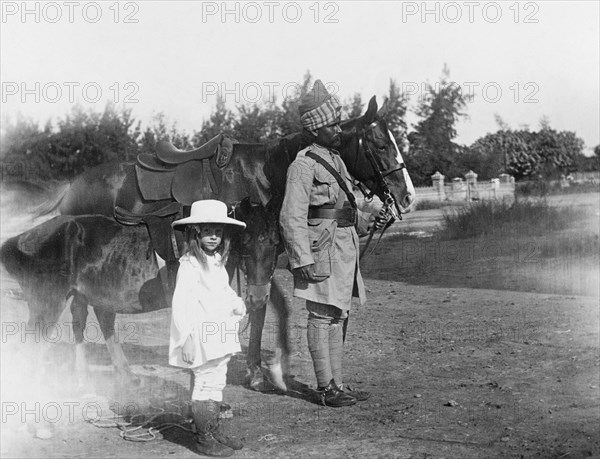 Margaret Lawrence with a 'sowar' . Margaret Lawrence (b.1904), the daughter of Phyllis and Sir Henry Staveley Lawrence (Collector of Karachi), holds the reigns of a small pony as she stands beside a turbaned 'sowar' (cavalry soldier) of the Indian Army. Karachi, India (Pakistan), circa 1912. Karachi, Sindh, Pakistan, Southern Asia, Asia.