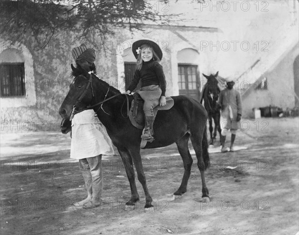 Riding a pony led by a 'sowar'. Margaret Lawrence (b.1904), the daughter of Phyllis and Sir Henry Staveley Lawrence (Collector of Karachi), rides a pony led by a turbaned 'sowar' (cavalry soldier) of the Indian Army. Karachi, India (Pakistan), circa 1912. Karachi, Sindh, Pakistan, Southern Asia, Asia.