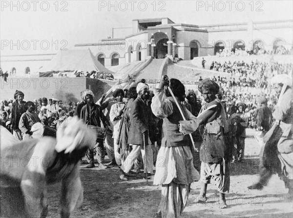 A display of swordsmanship. Musicians play as two swordsmen spar at an outdoor event. Sukkur, Sind, India (Sindh, Pakistan), circa 1908. Sukkur, Sindh, Pakistan, Southern Asia, Asia.