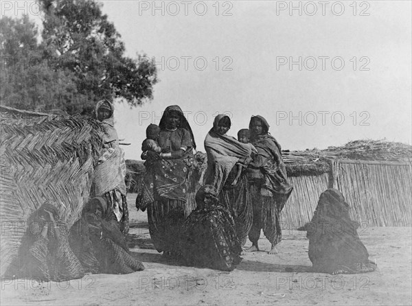 Indian women from a rural village. Portrait of a group of Indian women in a rural Indian village, two of whom hold babies. All wear traditional north east Indian dress including patterned robes and headscarves. Sukkur, Sind, India (Sindh, Pakistan), circa 1908. Sukkur, Sindh, Pakistan, Southern Asia, Asia.