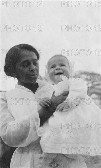 Indian ayah with Betty. An Indian ayah (nursemaid) called Nannie holds up a smiling four month old baby, Betty, for the camera. Nannie worked for a British family (the Lawrences) in India, later moving with them to England where she lived for the rest of her life. India, circa 1920. India, Southern Asia, Asia.