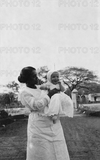 Indian ayah with Betty. An Indian ayah (nursemaid) called Nannie holds up a smiling four month old baby, Betty, for the camera. Nannie worked for a British family (the Lawrences) in India, later moving with them to England where she lived for the rest of her life. India, circa 1920. India, Southern Asia, Asia.