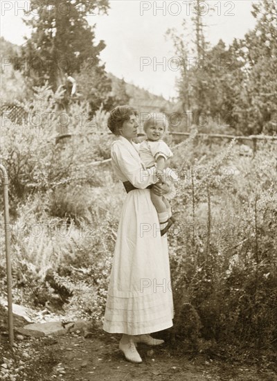 Rosamond Lawrence with Owen. Rosamond Lawrence, the second wife of Sir Henry Staveley Lawrence (Commissioner of Sind), holds a young boy, Owen, in her arms in an overgrown garden. India, circa 1916. India, Southern Asia, Asia.