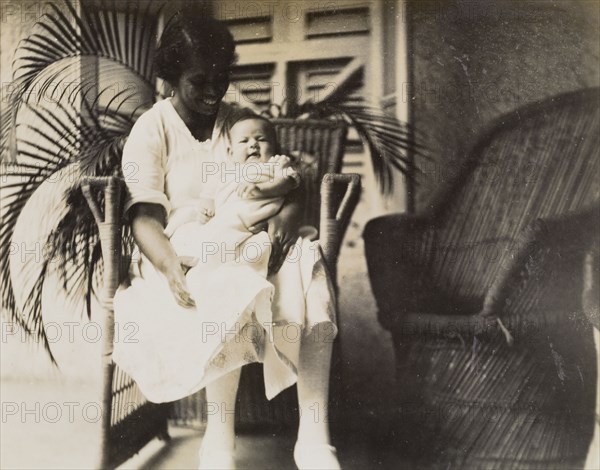 An Indian ayah with an infant. An Indian ayah (nursemaid) called Nannie sits on a veranda, cradling baby Mary Ann on her lap. Nannie worked for a British family (the Lawrences) in India, later moving with them to England where she lived for the rest of her life. India, circa 1920. India, Southern Asia, Asia.