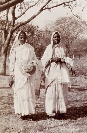 Indian women wearing saris. Portrait of two Indian women wearing traditional saris. One holds a Western-style straw hat in her hand. Karachi, Sind, India (Sindh, Pakistan), circa 1910. Karachi, Sindh, Pakistan, Southern Asia, Asia.