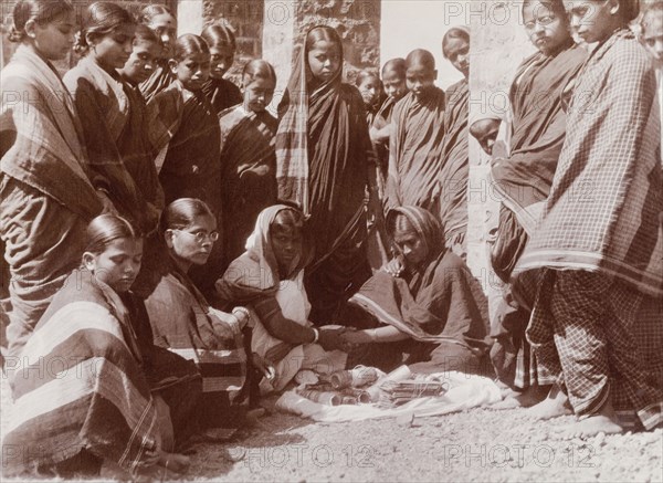 Women trying on bracelets. A group of Indian women in saris gather around a street vendor who sells a variety of bracelets from a mat on the ground. Karachi, Sind, India (Sindh, Pakistan), circa 1910. Karachi, Sindh, Pakistan, Southern Asia, Asia.