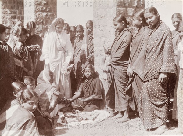 Women trying on bracelets. A group of Indian women in saris gather around a street vendor who sells a variety of bracelets from a mat on the ground. Karachi, Sind, India (Sindh, Pakistan), circa 1910. Karachi, Sindh, Pakistan, Southern Asia, Asia.