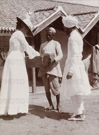 Phyllis Lawrence visits stables in Karachi. Phyllis Louise Lawrence, the first wife of Sir Henry Staveley Lawrence (Collector of Karachi), reaches into a wooden box offered to her by an Indian attendant at farm stables in Karachi. Karachi, Sind, India (Sindh, Pakistan), circa 1910. Karachi, Sindh, Pakistan, Southern Asia, Asia.