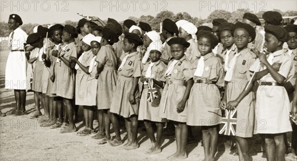 Brownies awaiting the arrival of Queen Elizabeth II. A pack of Nigerian Brownies stand in line holding union jack flags as they await the arrival of Queen Elizabeth. Kaduna, Nigeria, February 1956. Kaduna, Kaduna, Nigeria, Western Africa, Africa.