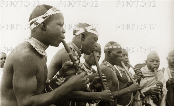 Nigerian pipe players. A group of Nigerian musicians gather to play pipes. Naked from the waist up, they wear decorative headbands around their shaven heads and are adorned with beaded necklaces and armbands. Nigeria, circa 1955. Nigeria, Western Africa, Africa.