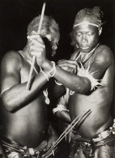Two Nigerian dancers. Night portrait of two male Nigerian dancers. Naked from the waist up, one man adjusts the other's fur armband. Nigeria, circa 1948. Nigeria, Western Africa, Africa.