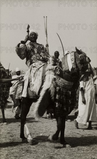 Nigerian chief on a caparisoned horse. A Nigerian chief poses with a spear in his hand as he rides a caparisoned horse during celebrations for Sallah, an Islamic event held to mark the end of Ramadan. Nigeria, circa 1948. Nigeria, Western Africa, Africa.