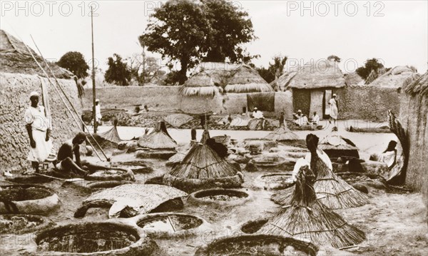 Dye wells in Zaria. Textile workers sit outdoors, dipping lengths of fabric into wells of dye, probably indigo. Several unused wells are covered with basketwork lids as protection against the sun. Zaria, Nigeria, circa 1940. Zaria, Kaduna, Nigeria, Western Africa, Africa.