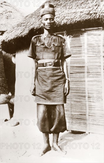 A Nigerian policeman at Minna. A uniformed Nigerian policeman stands outside a thatched village hut, posing for the camera with his hands by his sides. Minna, Nigeria, circa 1940. Minna, Niger, Nigeria, Western Africa, Africa.