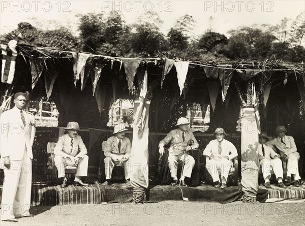 Colonial officers at the Obuasi Durbar. British colonial officers, including Sir Alan Burns (1887-1980), Governor of the Gold Coast (centre), sit on a dais decorated with British flags at the Obuasi Durbar. Obuasi, Asante, Gold Coast (Ghana), 1943. Obuasi, Ashanti, Ghana, Western Africa, Africa.