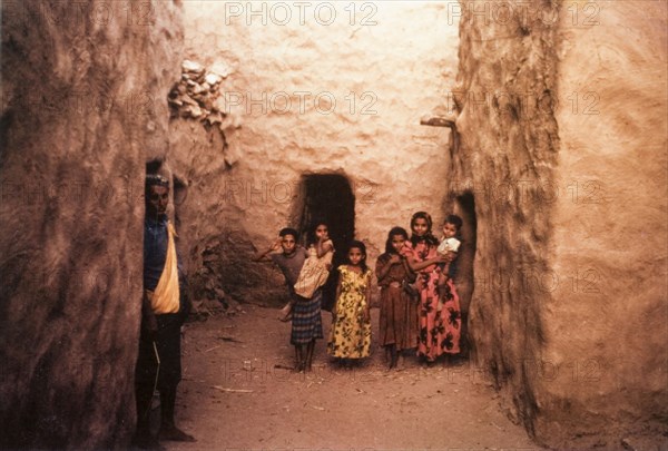 A group of children in Yemen. A group of children pose for the camera in an alcove formed by mud-walled buildings. Lodar, Yemen, circa 1963., Abyan, Yemen, Middle East, Asia.