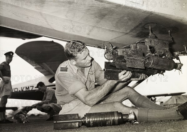Kenya Police Airwing officer attaches missiles. Ian Cuthbert, an officer of the Kenya Police Airwing, attaches a small missile to the underside of an aircraft. Kenya, circa 1955. Kenya, Eastern Africa, Africa.