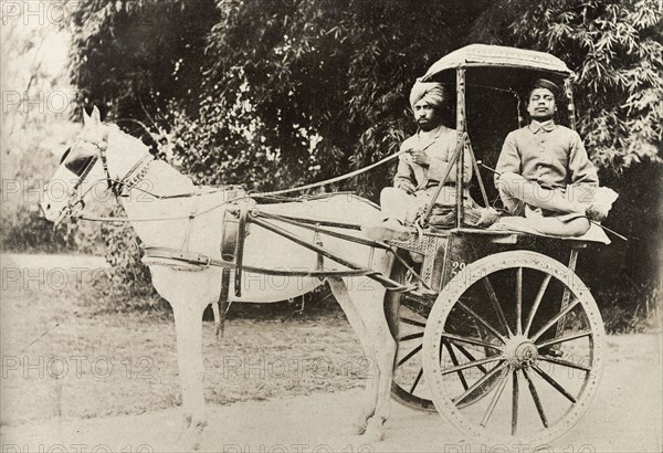 A horse-drawn tonga. An Indian driver and his passenger sit cross-legged on a horse-drawn tonga. India, circa 1915. India, Southern Asia, Asia.