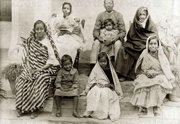 Portrait of an Indian family. Group portrait of an Indian family wearing traditional dress. Four sisters sit at the front with their parents and grandmother behind them holding a toddler and a baby. India, circa 1920. India, Southern Asia, Asia.