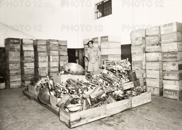 Confiscated opium equipment. An officer of the Singapore Police stands over a haul of confiscated opium equipment in a police warehouse. Singapore, circa 1950. Singapore, Central (Singapore), Singapore, South East Asia, Asia.