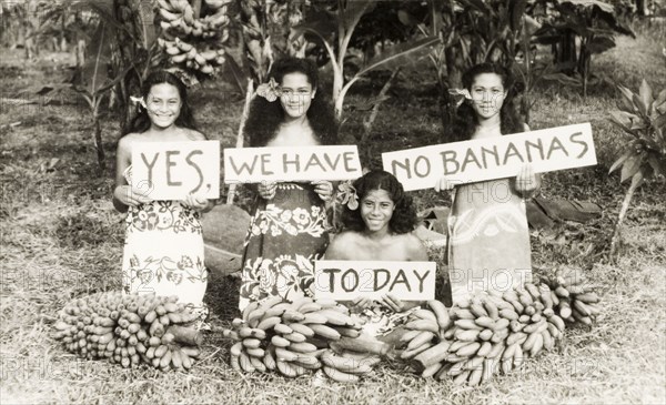 Yes, we have no bananas today'. Four young Samoan women kneel on a patch of grass behind several hands of bananas, holding up signs that read: 'Yes, we have no bananas today'. The phrase was popularised by a song of the same name, which was written by Irving Cohn and Frank Silver in 1923. Apia, Western Samoa (Samoa), circa 1956. Apia, Apia Urban Area, Samoa, Pacific Ocean, Oceania.