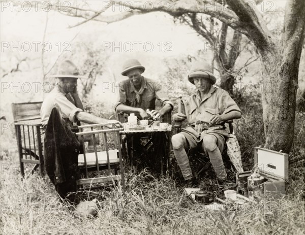 Prince Edward of Wales on safari. Prince Edward of Wales (right), later King Edward VIII, sits at a table beneath a tree, drinking tea with two companions whilst on safari in Tanganyika. Tanganyika Territory (Tanzania), 1927. Tanzania, Eastern Africa, Africa.