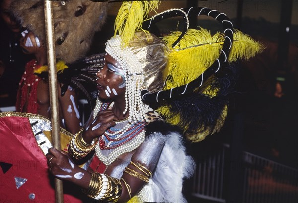 Carnival costume at the Commonwealth Institute. Profile shot of a child wearing elaborate costume for a carnival held at the Commonwealth Institute. Decorated with face and body paint, he wears a large feathered headdress and strings of beads around his head and neck. London, England, circa 1985. London, London, City of, England (United Kingdom), Western Europe, Europe .