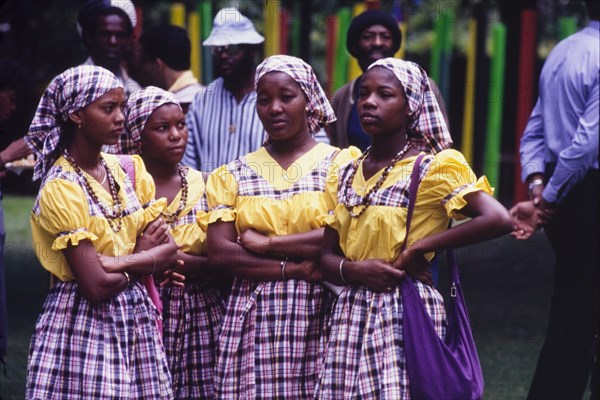 Dancers at the Caribbean Music Village. Four female dancers stand with their arms crossed as they await their performance at the Caribbean Music Village, a cultural festival held at the Commonwealth Institute. They wear matching costumes comprising checked headscarfs and skirts with yellow shirts. London, England, 7-26 July 1986. London, London, City of, England (United Kingdom), Western Europe, Europe .
