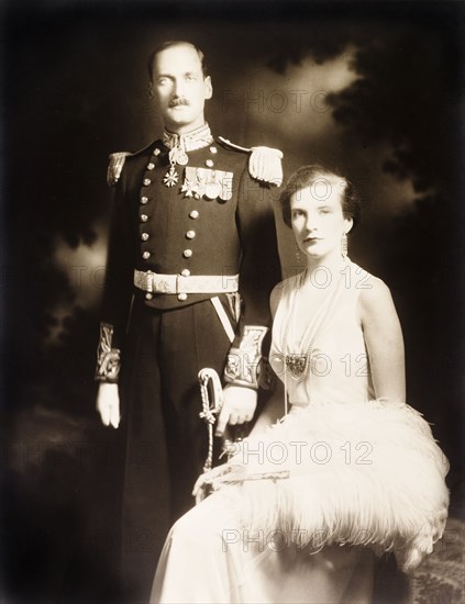 Sir Bede and Lady Clifford. Studio portrait of Sir Bede Edmund Hugh Clifford, Governor of the Bahamas, and his wife, Lady Clifford. The couple are dressed in formal attire: Sir Bede in full military regalia, his wife in a white evening gown with an ostrich feather fan. Bahamas, circa 1932. Bahamas, Atlantic Ocean, Africa.
