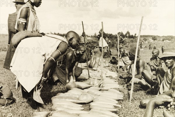 Gourd stall at Karatina market. Shoppers haggle with Kikuyu traders over slender, hollow gourds at Karatina market. An original caption comments that these gourds were "much in demand for keeping beans...and witchdoctors potions". South Nyeri, Kenya, 1936. Nyeri, Central (Kenya), Kenya, Eastern Africa, Africa.